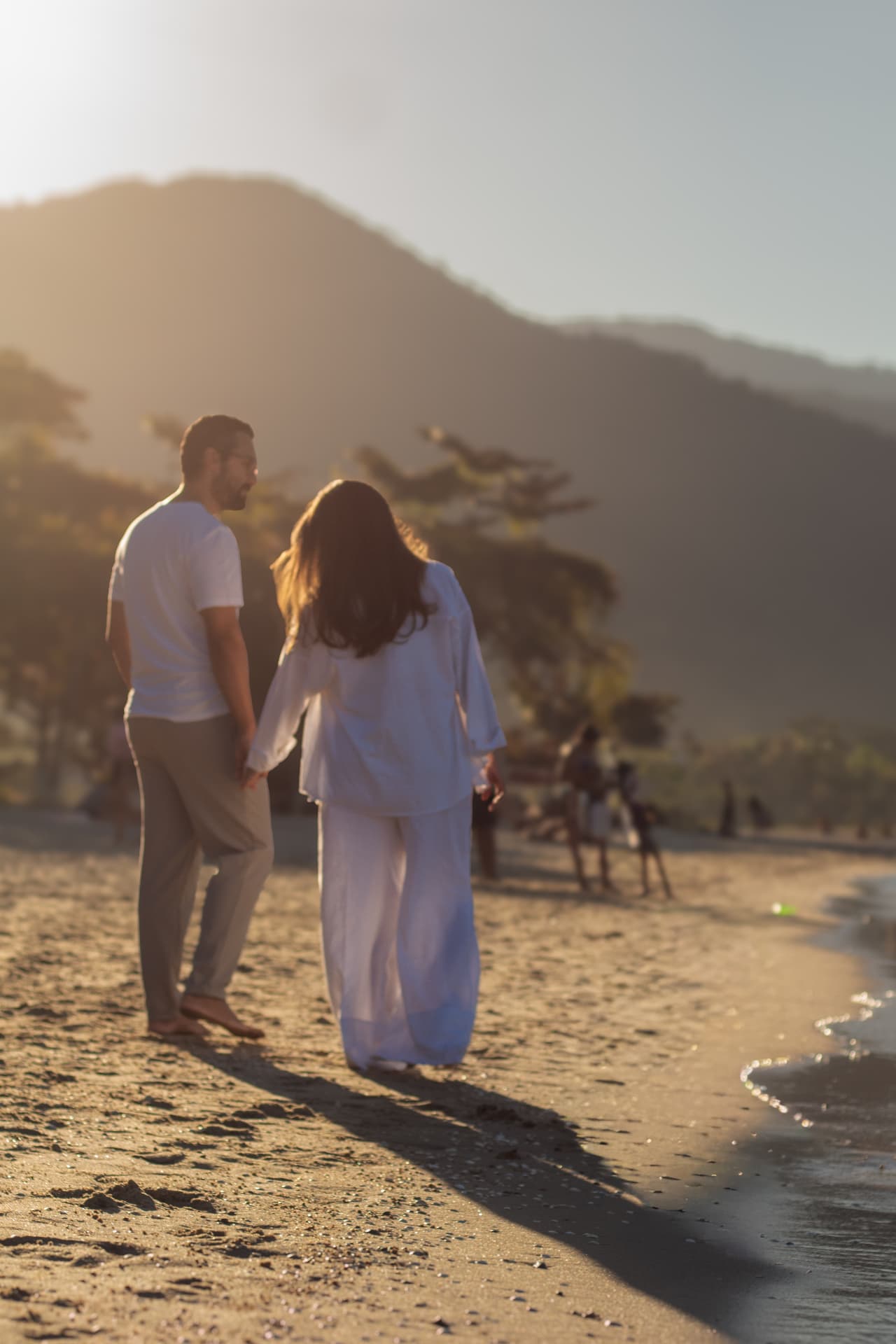 Ensaio gestante — casal caminhando na praia ao entardecer