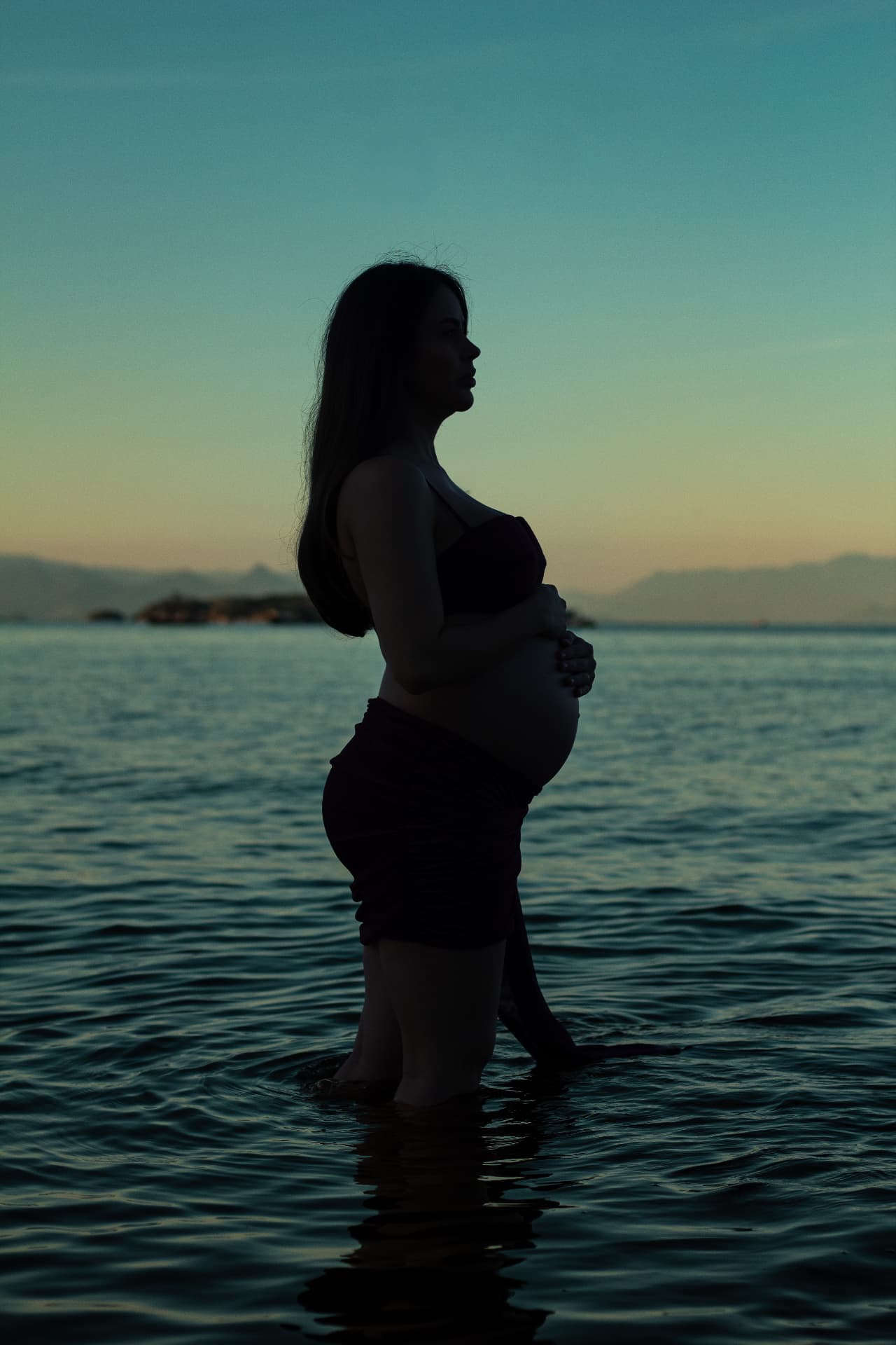 Ensaio gestante — silhueta na água ao pôr do sol